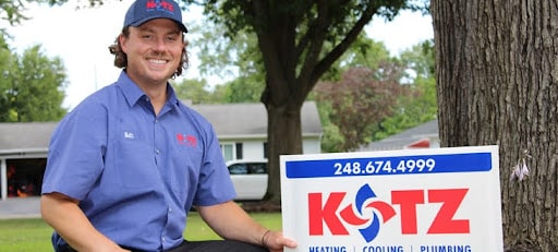 kotz heating cooling and plumbing technician with yard sign with kotz logo